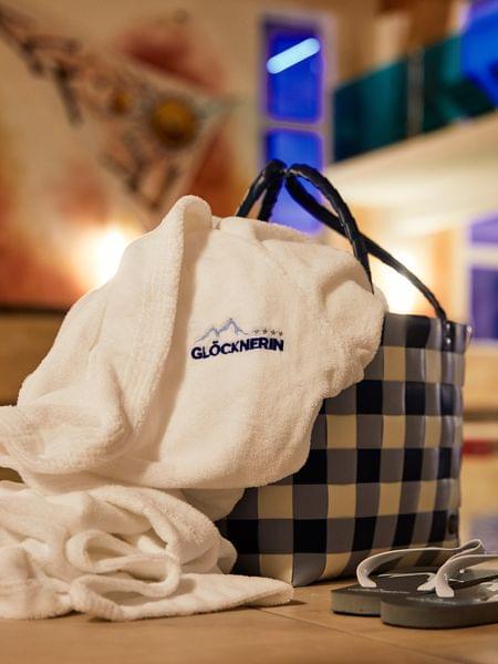 Hotel-Highlights & Inklusivleistungen Wellness-Bademantel mit Glocknerin-Logo neben Korb und Flip-Flops am Innenpool
